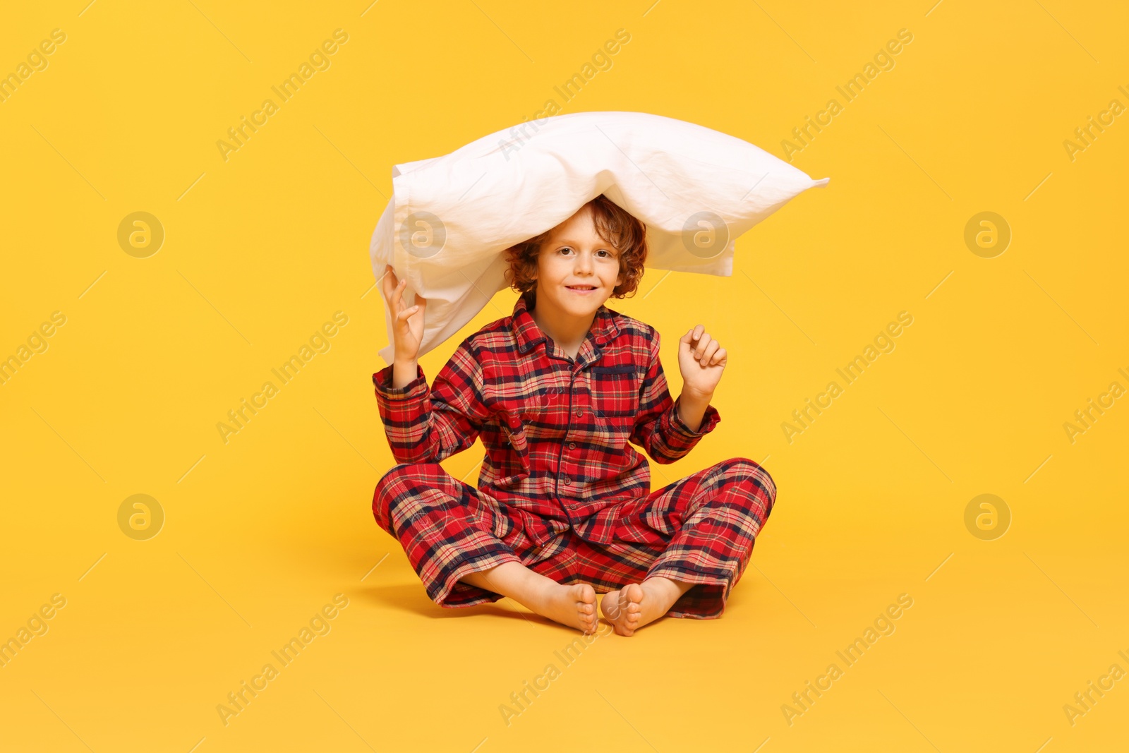 Photo of Cute little boy in pajamas with pillow on yellow background