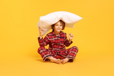 Photo of Cute little boy in pajamas with pillow on yellow background