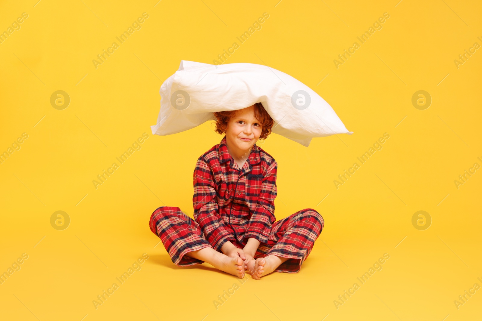 Photo of Cute little boy in pajamas with pillow on yellow background