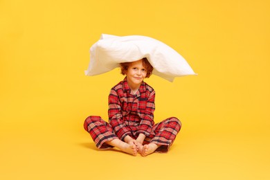Photo of Cute little boy in pajamas with pillow on yellow background