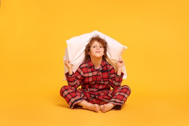 Photo of Cute little boy in pajamas with pillow on yellow background