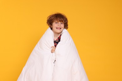 Photo of Cute little boy in pajamas with blanket on yellow background