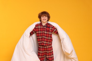 Photo of Cute little boy in pajamas with blanket on yellow background