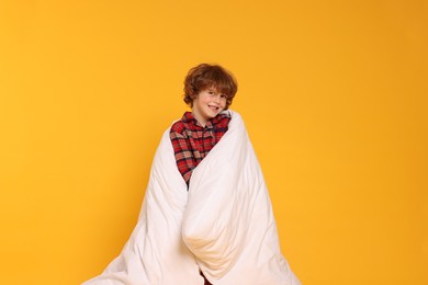 Photo of Cute little boy in pajamas with blanket on yellow background