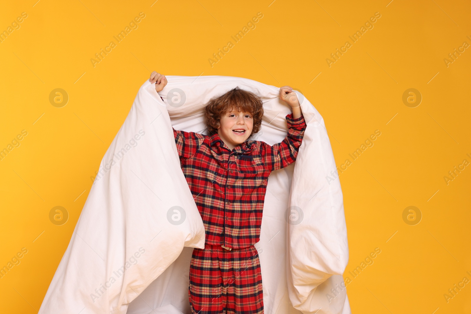 Photo of Cute little boy in pajamas with blanket on yellow background