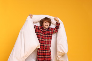 Photo of Cute little boy in pajamas with blanket on yellow background