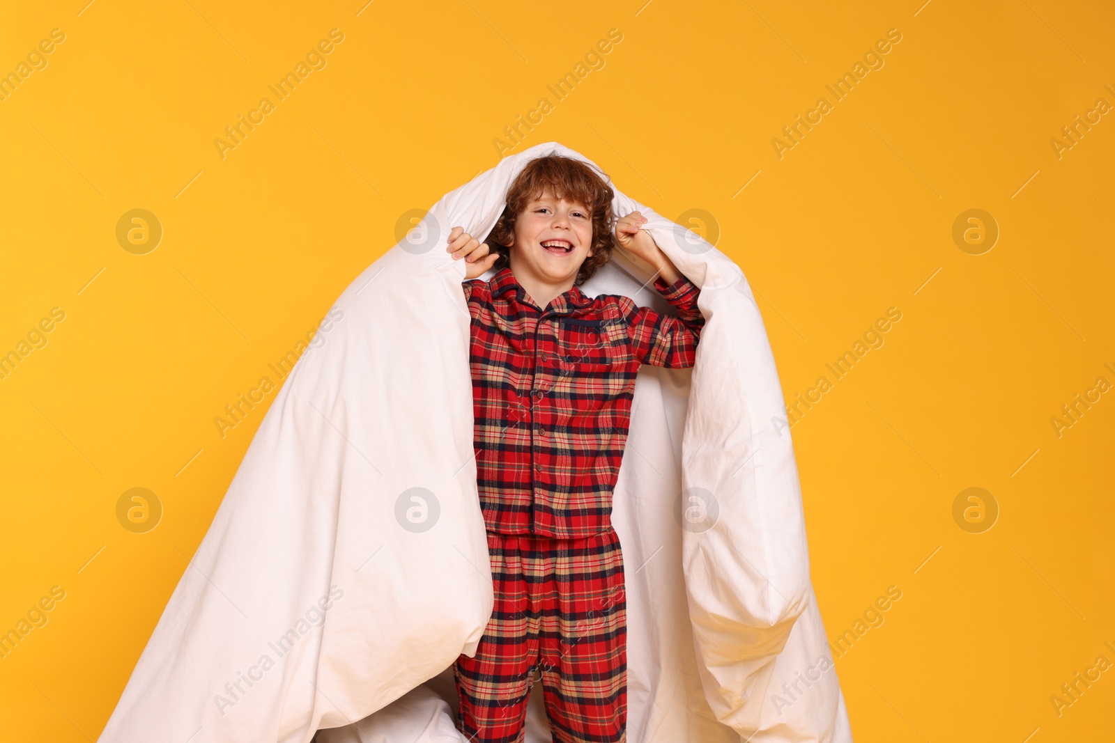 Cute little boy in pajamas with blanket on yellow background Photo of Cute little boy in pajamas with blanket on yellow background