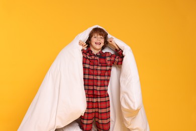 Photo of Cute little boy in pajamas with blanket on yellow background