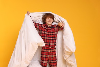 Photo of Cute little boy in pajamas with blanket on yellow background