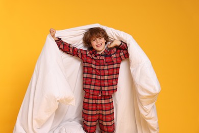 Photo of Cute little boy in pajamas with blanket on yellow background