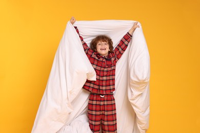 Photo of Cute little boy in pajamas with blanket on yellow background