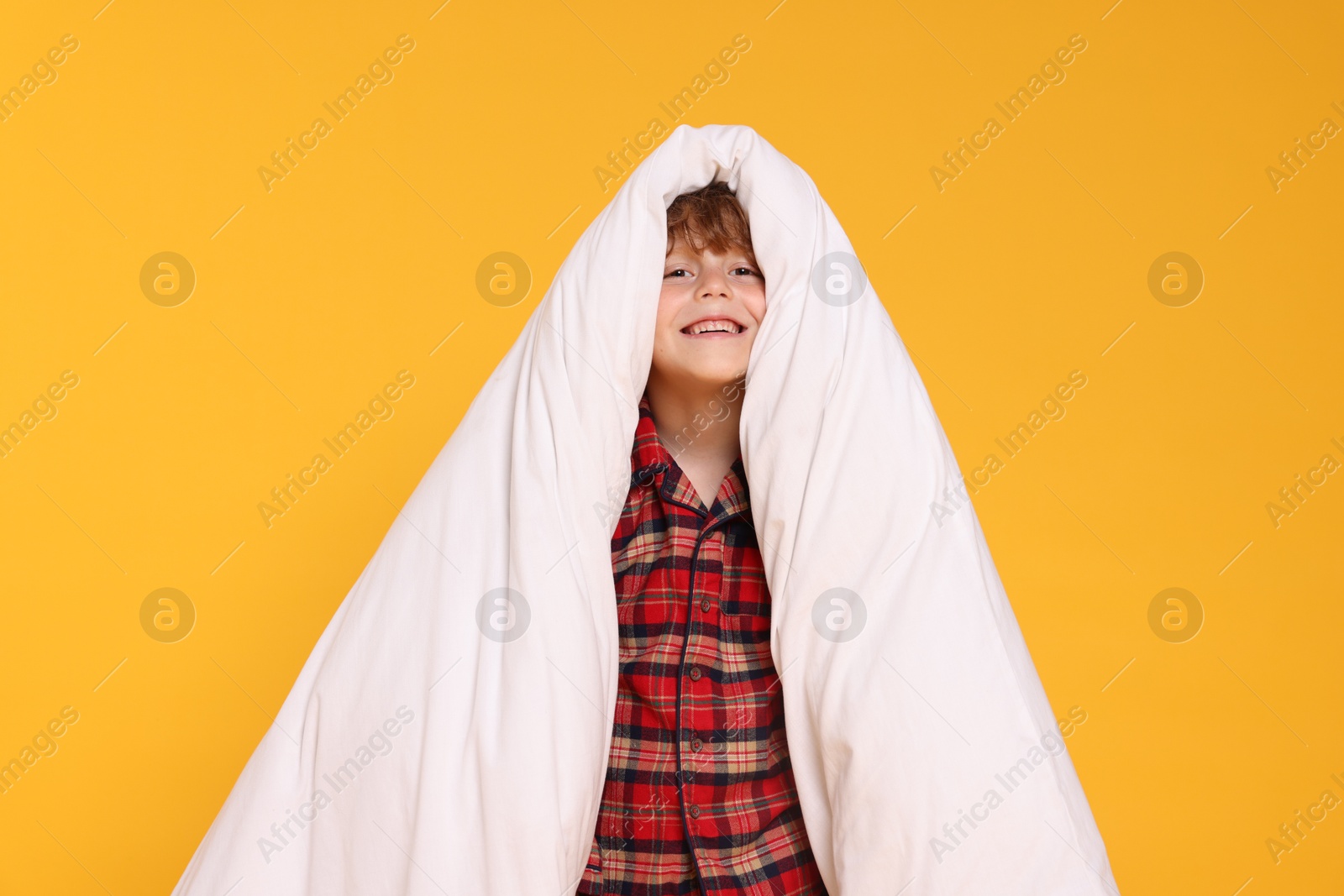 Photo of Cute little boy in pajamas with blanket on yellow background