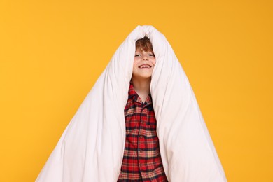 Photo of Cute little boy in pajamas with blanket on yellow background