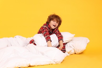 Photo of Cute little boy in pajamas with pillow and blanket on yellow background