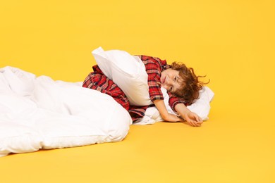 Photo of Cute little boy in pajamas with pillow and blanket on yellow background