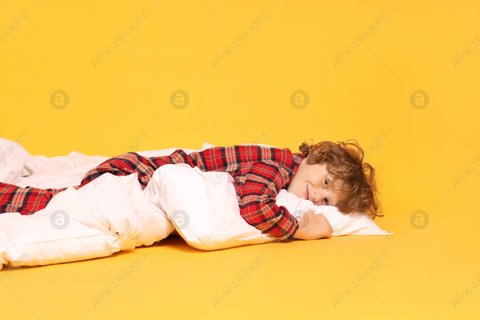 Photo of Cute little boy in pajamas with pillow and blanket on yellow background