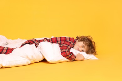 Photo of Cute little boy in pajamas with pillow and blanket on yellow background