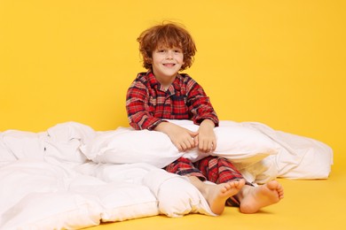 Photo of Cute little boy in pajamas with pillow and blanket on yellow background