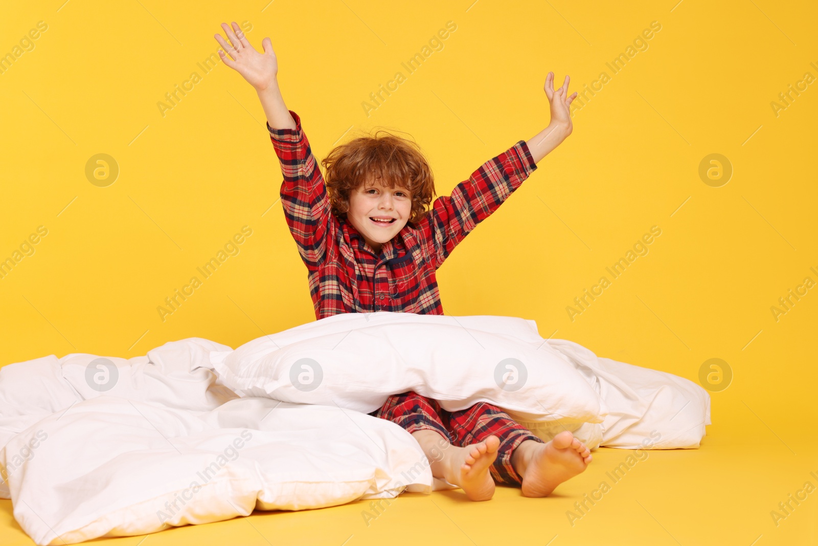 Cute little boy in pajamas with pillow and blanket on yellow background Photo of Cute little boy in pajamas with pillow and blanket on yellow background
