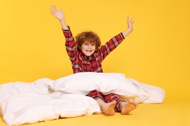 Photo of Cute little boy in pajamas with pillow and blanket on yellow background