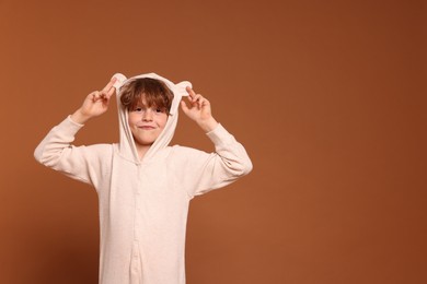 Photo of Cute little boy in pajamas on brown background. Space for text