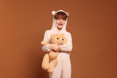 Photo of Cute little boy in pajamas with teddy bear on brown background