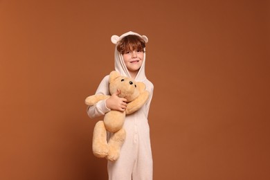 Photo of Cute little boy in pajamas with teddy bear on brown background