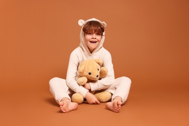 Photo of Cute little boy in pajamas with teddy bear on brown background