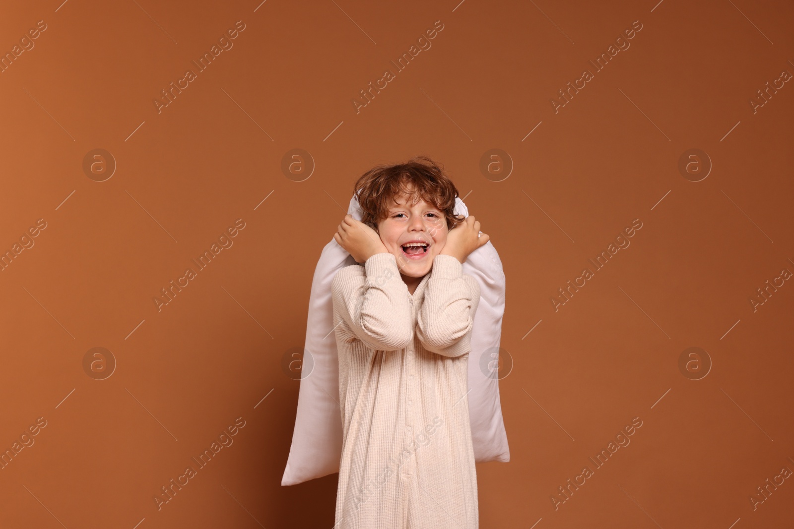 Cute little boy in pajamas with pillow on brown background Photo of Cute little boy in pajamas with pillow on brown background