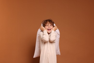 Photo of Cute little boy in pajamas with pillow on brown background