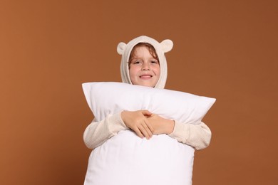 Photo of Cute little boy in pajamas with pillow on brown background
