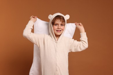 Photo of Cute little boy in pajamas with pillow on brown background
