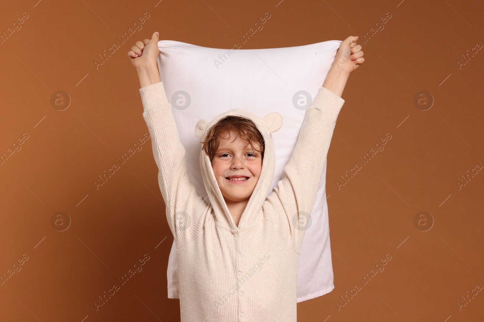 Cute little boy in pajamas with pillow on brown background Photo of Cute little boy in pajamas with pillow on brown background