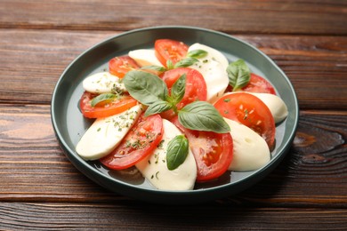 Photo of Tasty salad Caprese with mozzarella, tomatoes, basil and spices on wooden table, closeup