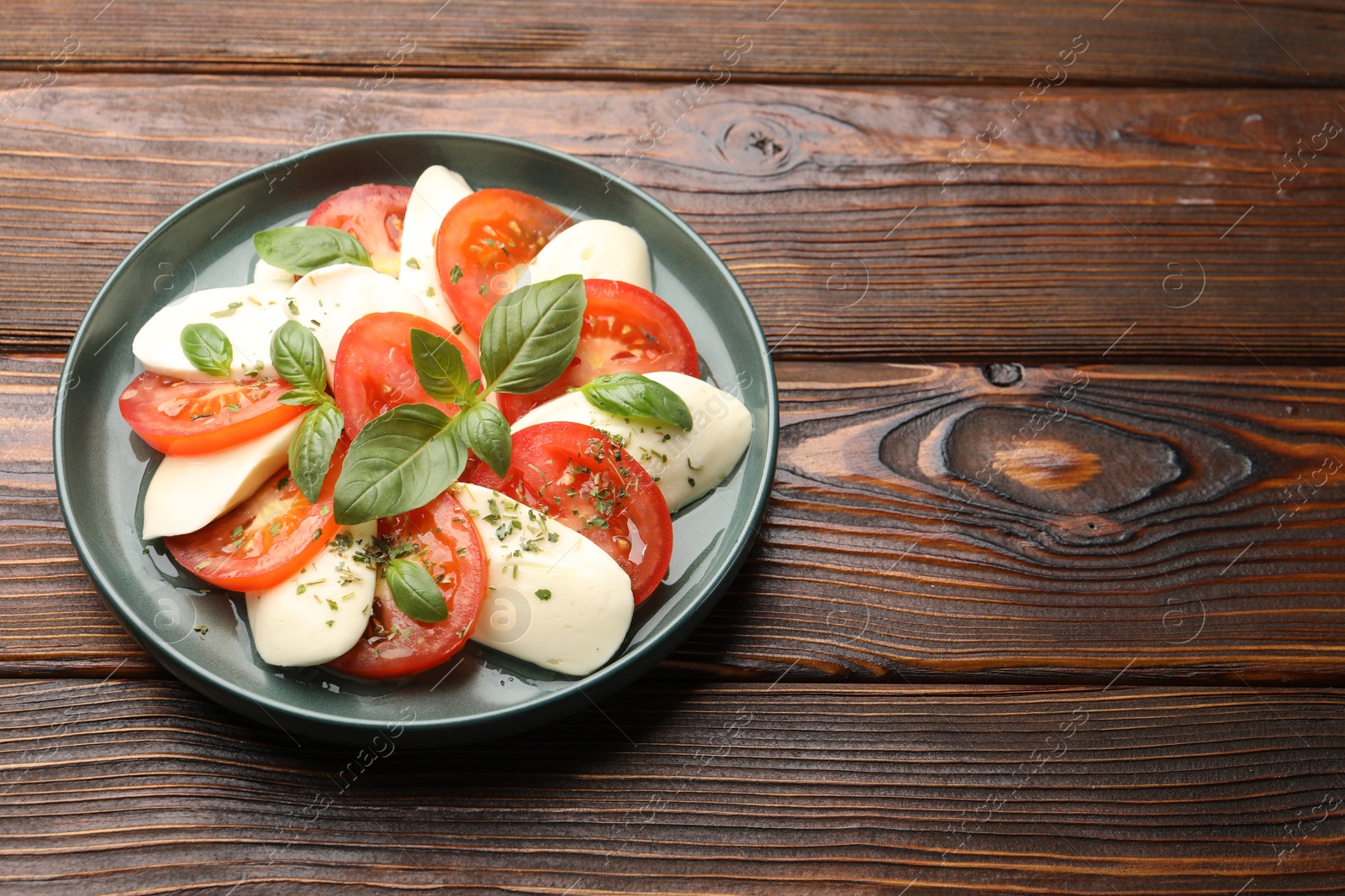 Tasty salad Caprese with mozzarella, tomatoes, basil and spices on wooden table. Space for text Photo of Tasty salad Caprese with mozzarella, tomatoes, basil and spices on wooden table. Space for text