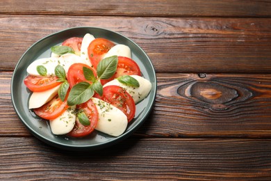 Photo of Tasty salad Caprese with mozzarella, tomatoes, basil and spices on wooden table. Space for text