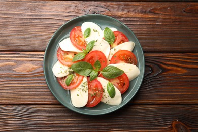 Photo of Tasty salad Caprese with mozzarella, tomatoes, basil and spices on wooden table, top view