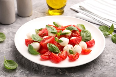 Photo of Tasty salad Caprese with mozzarella, tomatoes, basil and spices on grey table, closeup