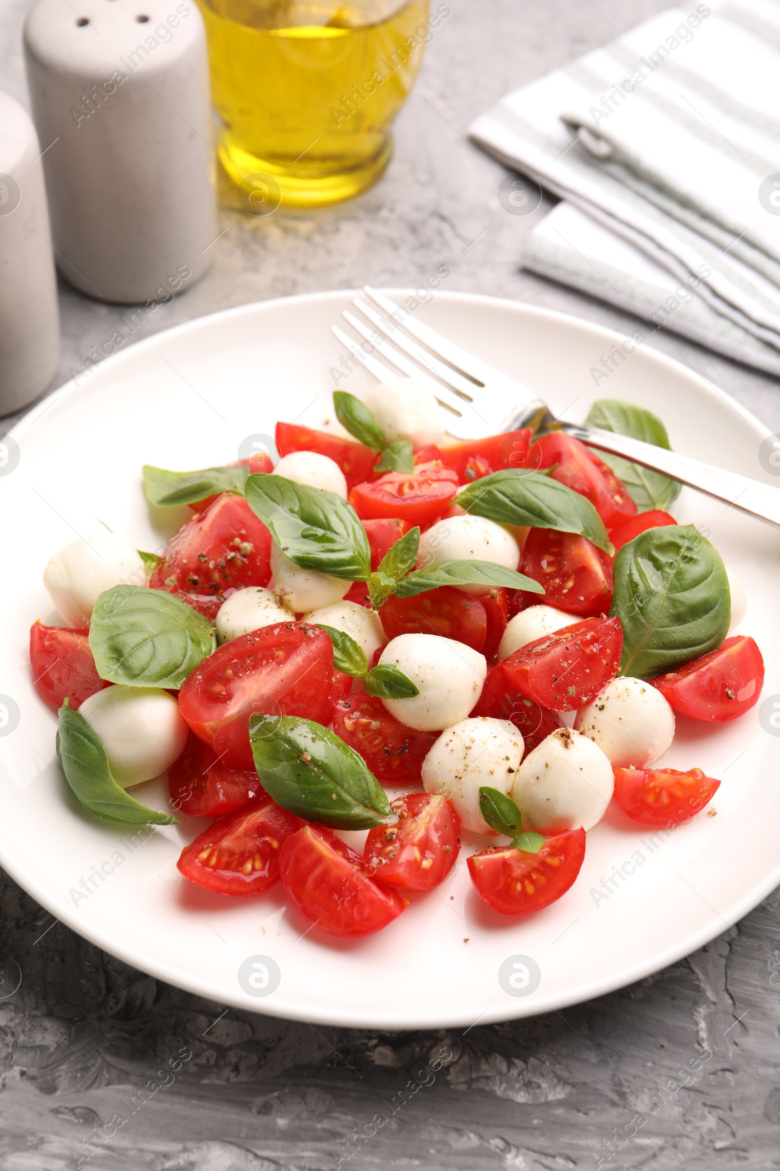 Tasty salad Caprese with mozzarella, tomatoes, basil and spices on grey table, closeup Photo of Tasty salad Caprese with mozzarella, tomatoes, basil and spices on grey table, closeup