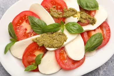 Photo of Tasty salad Caprese with mozzarella, tomatoes, basil and pesto sauce on grey table, top view