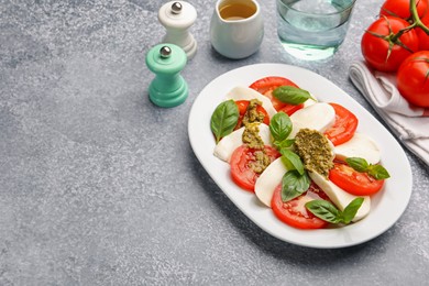 Photo of Tasty salad Caprese served with pesto sauce on grey table. Space for text