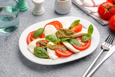 Photo of Tasty salad Caprese served with pesto sauce on grey table, closeup