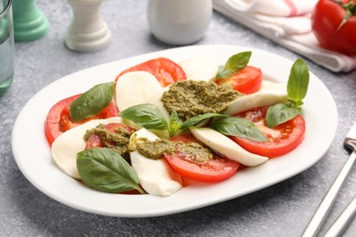 Photo of Tasty salad Caprese served with pesto sauce on grey table, closeup