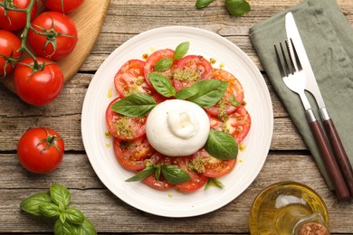 Photo of Tasty salad Caprese served with pesto sauce on wooden table, flat lay