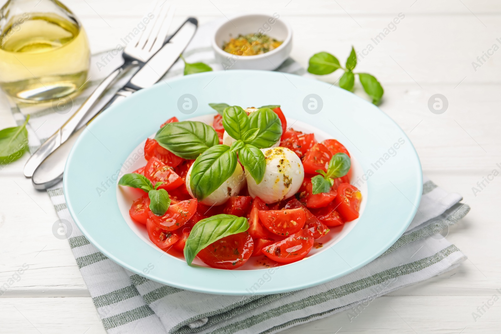 Tasty salad Caprese with mozzarella, tomatoes, basil and spices on white wooden table, closeup Photo of Tasty salad Caprese with mozzarella, tomatoes, basil and spices on white wooden table, closeup