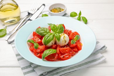 Photo of Tasty salad Caprese with mozzarella, tomatoes, basil and spices on white wooden table, closeup