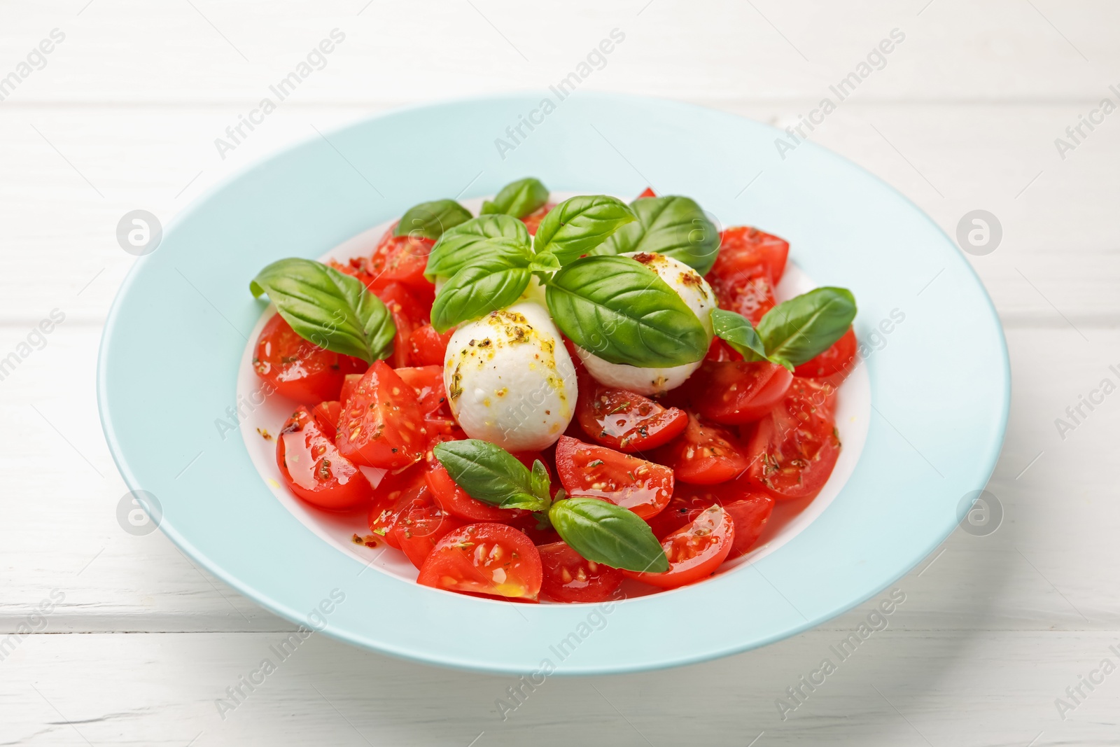 Tasty salad Caprese with mozzarella, tomatoes, basil and spices on white wooden table, closeup Photo of Tasty salad Caprese with mozzarella, tomatoes, basil and spices on white wooden table, closeup