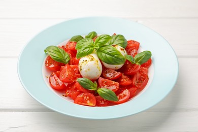 Photo of Tasty salad Caprese with mozzarella, tomatoes, basil and spices on white wooden table, closeup