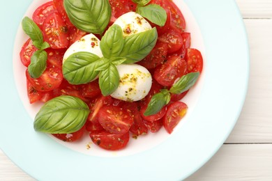 Photo of Tasty salad Caprese with mozzarella, tomatoes, basil and spices on white wooden table, top view