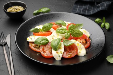 Photo of Tasty salad Caprese with mozzarella, tomatoes, basil and spices on black table, closeup